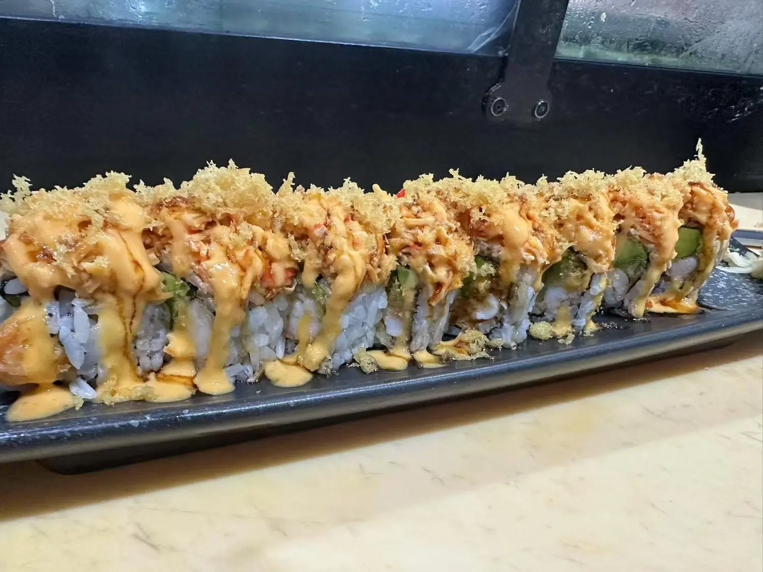 Sushi roll topped with crispy tempura bits, spicy mayo, and avocado, offering a crunchy and zesty flavor at Hibachi Express & Sushi, a Japanese restaurant in Oklahoma City